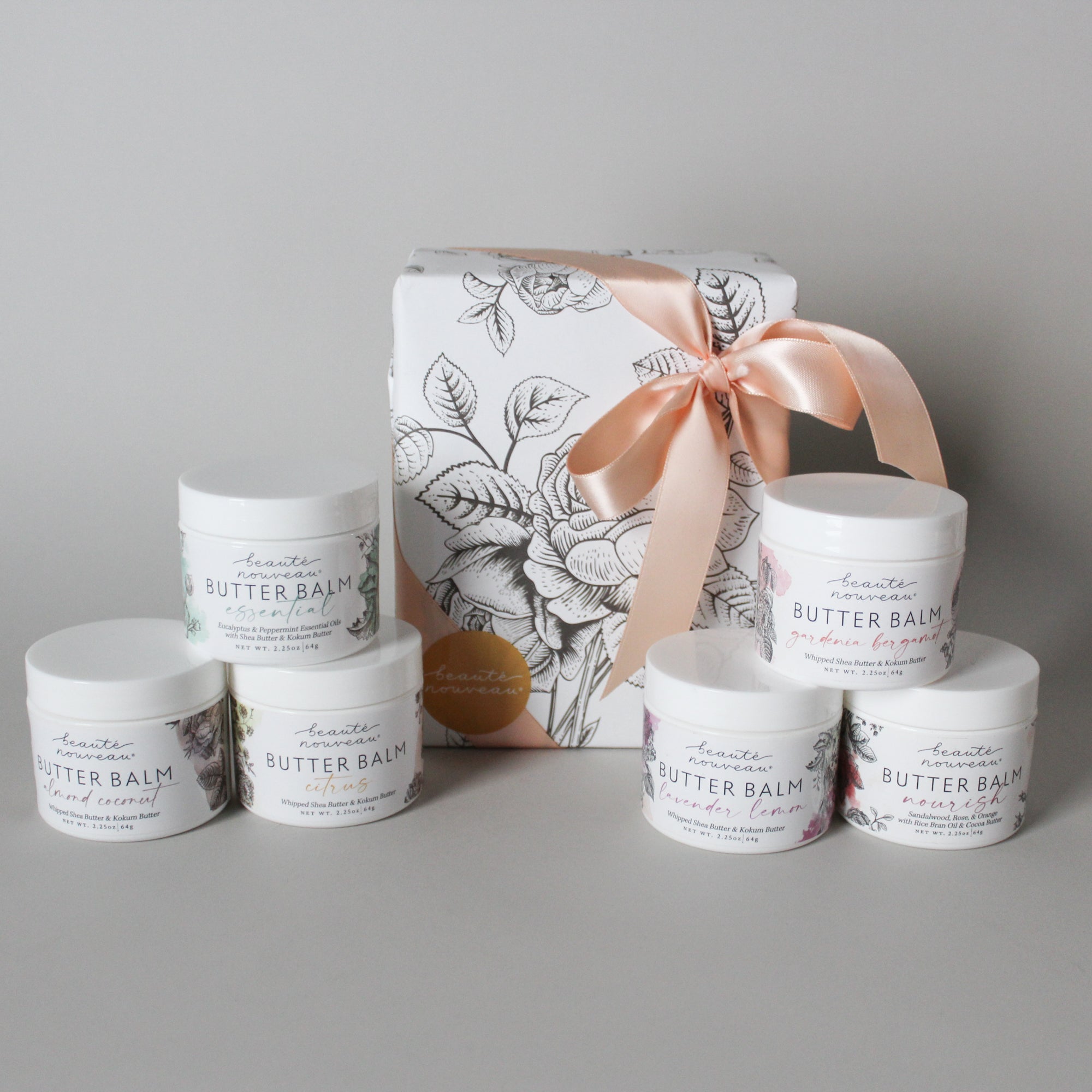 size petite butter balms in white plastic jars with floral labels and a beautifully wrapped package with pink ribbon
