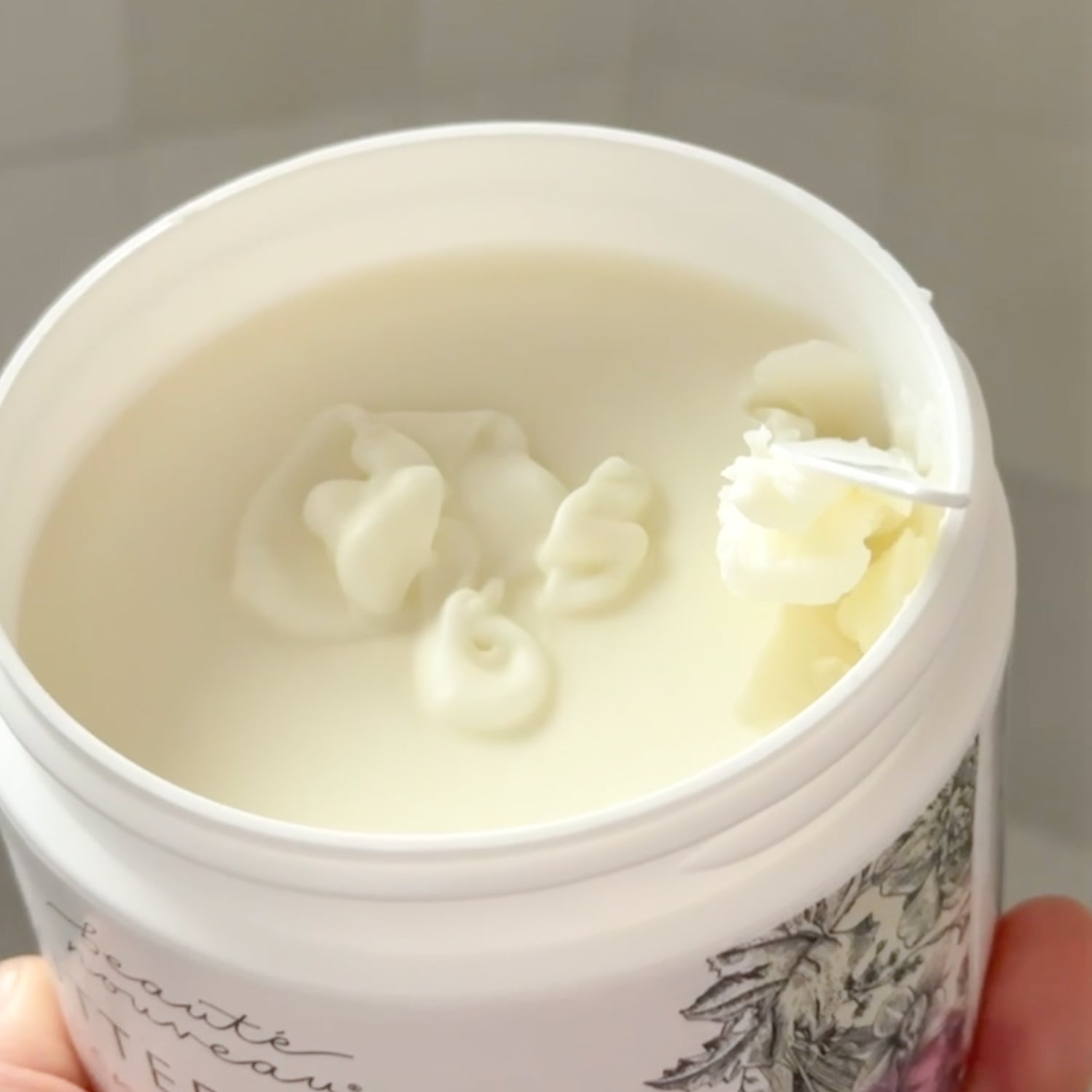 Close-up of an all-natural butter balm container with a floral design on a neutral background
