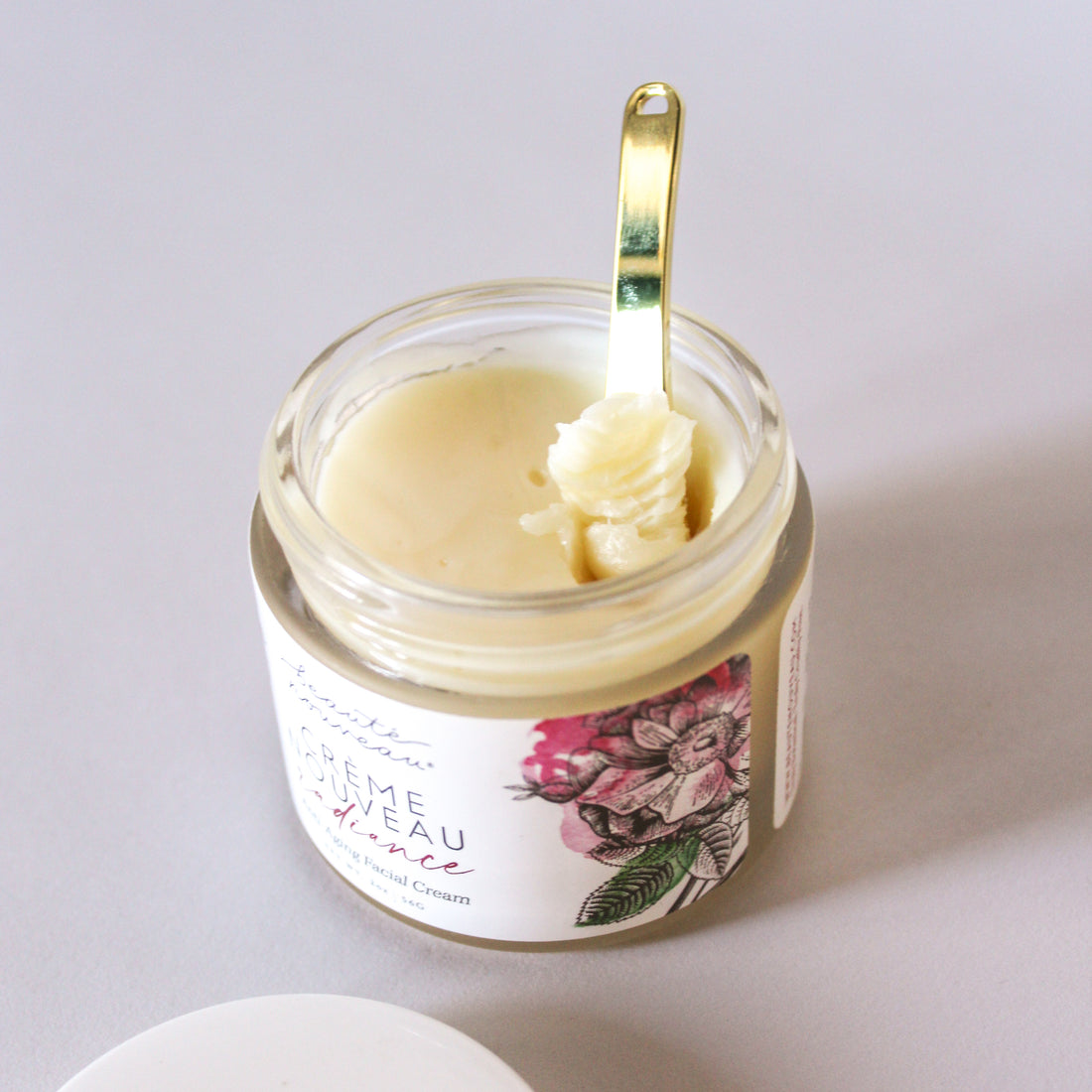 A close up of an open jar of Creme Nouveau with gold scoop.