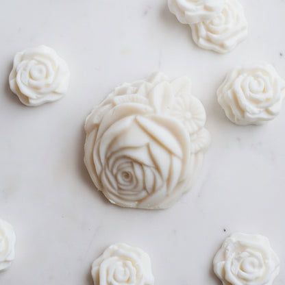 A styled flat-lay of Shea Milk Bar Facial Soap showing several sculpted off-white rose-shaped soaps on a white marble surface.